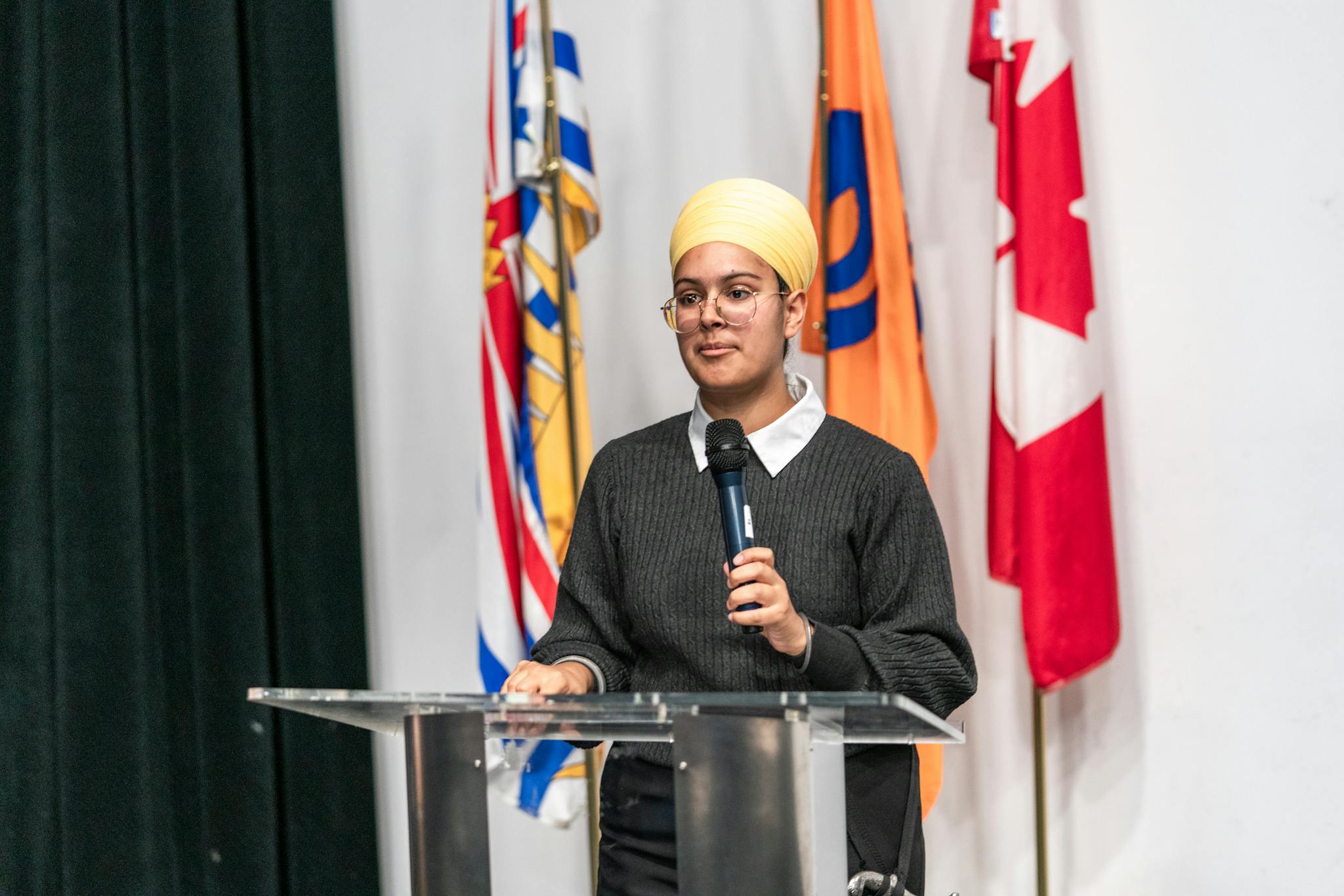 A young woman wearing a turban speaks at a podium with international flags in the background.