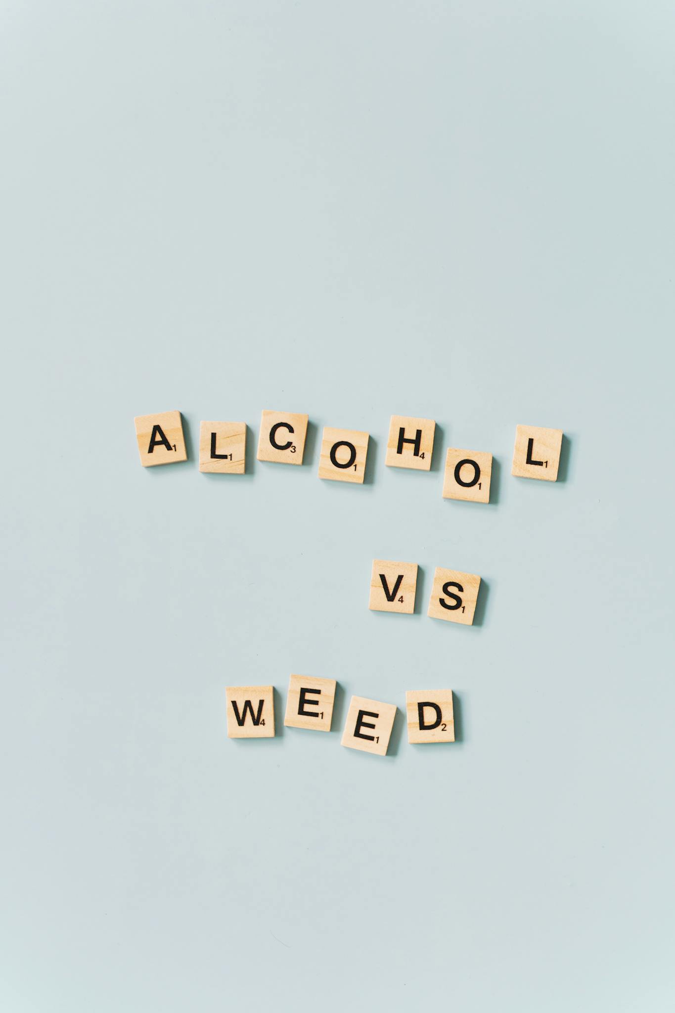Scrabble tiles spelling 'Alcohol vs Weed' on a light blue background.